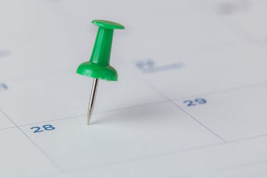 Selective focus of a green push pin marking on calendar for the concept of appointment, reminder and important note.