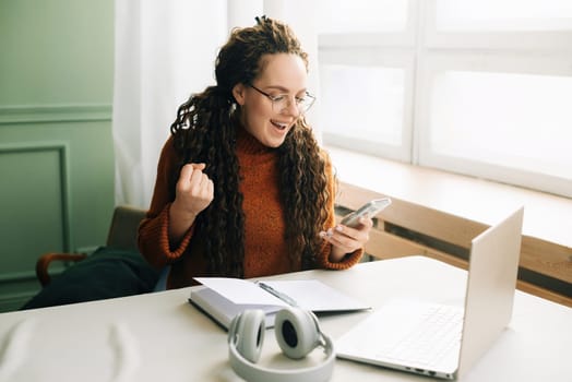 Young happy lucky woman student feeling excited winner holding cellphone using mobile phone winning online, receiving great news or sms offers on a smartphone, getting a new job celebrating success