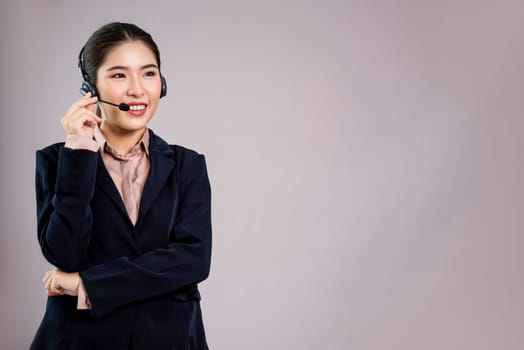 Attractive asian female call center operator with happy smile face advertises job opportunity on empty space, wearing a formal suit and headset on customizable isolated background. Enthusiastic