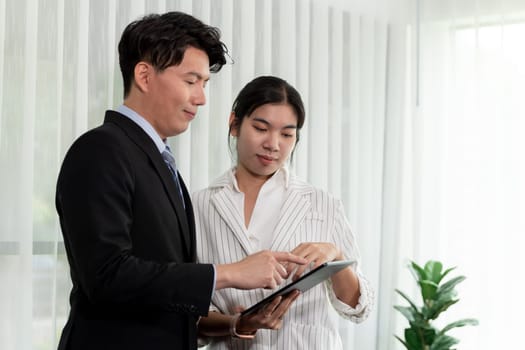 Manager advising guiding younger colleague with tablet in workplace. Couple businesspeople in formal wear working together on financial strategy as concept of teamwork and harmony in office.