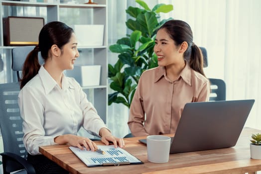 Two young office lady colleagues collaborating in modern office workspace, engaging in discussion and working together on laptop, showcasing their professionalism as modern office worker. Enthusiastic