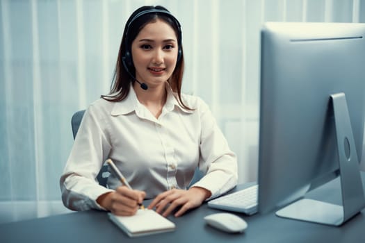 Asian call center with headset and microphone working on her workspace looking at camera. Female operator provide exceptional customer service. Supportive call center agent portrait. Enthusiastic