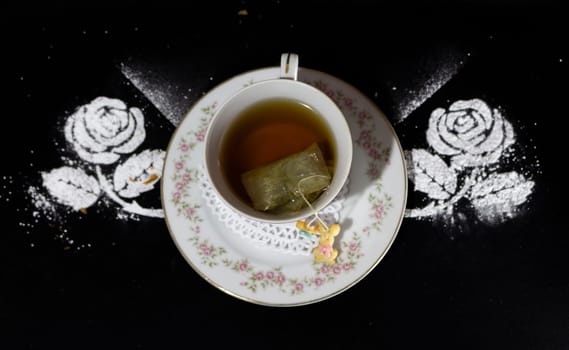 Antique porcelain tea cup seen from above with flowers, the tea bag inside and a small doll of candy growing, decorated with two powdered sugar flowers. High quality photo