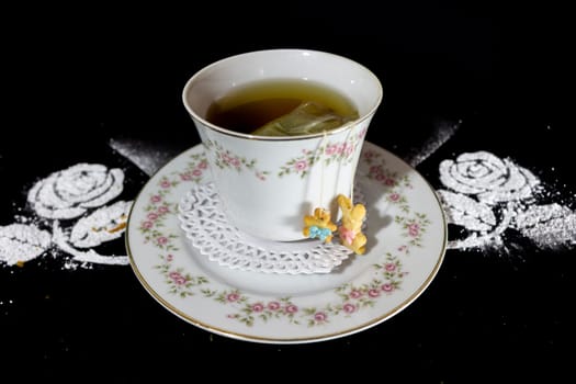 pastry plate: an old teacup with classic flowers, a pastry decoration of two small dolls and a black background. High quality photo