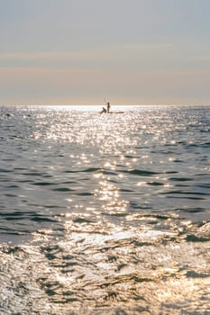 a couple of people on a board in the sea against the background of the rays of the sun. photo