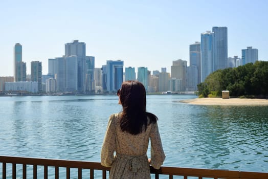 Cityscape of Sharjah UAE. A young woman in a long dress enjoys the view of skyscrapers and relaxing