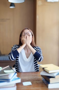 A portrait of an Asian teenage girl showing headaches and discouragement from studying in the library.