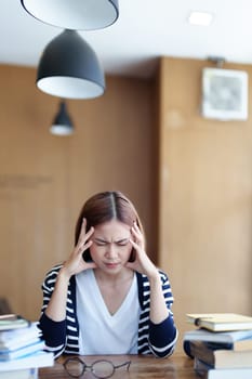 A portrait of an Asian teenage girl showing headaches and discouragement from studying in the library.