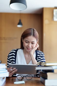 A portrait of a young Asian woman with a smiling face using a tablet computer during an online video conferencing class in a library.