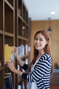 Portrait of a young Asian woman showing joy as she searches for knowledge in the library.