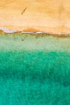 Aerial view of the walking people on the white sandy beach near sea with waves at sunset. Summer holiday. Top view of sporty people, clear azure water. Lifestyle and sport