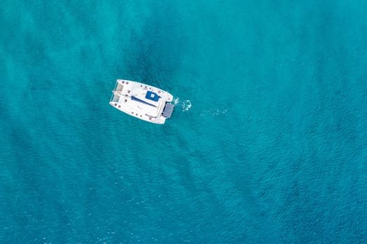 Aerial view of anchored sailing yacht in emerald sea. Aerial view of a boat. Outdoor water sports, yachting. Aerial view of anchoring yacht in open water. Ocean and sea travel and transportation