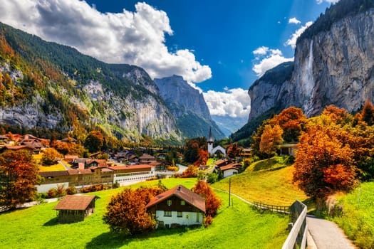 Captivating autumn view of Lauterbrunnen valley with gorgeous Staubbach waterfall and Swiss Alps at sunset time. Lauterbrunnen village with autumn red foliage, Berner Oberland, Switzerland, Europe.