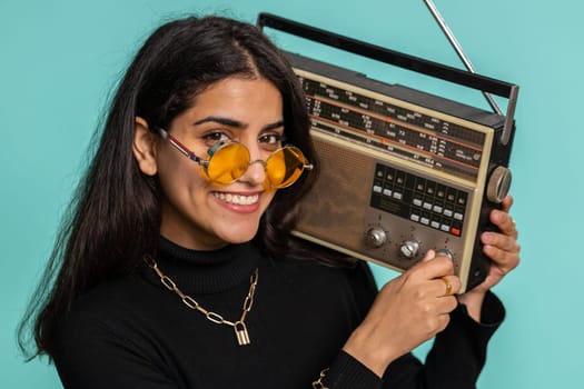 Indian woman using retro tape record player to listen music, disco dancing of favorite track, having fun, entertaining, fan of vintage technologies. Pretty hindu girl isolated on blue background