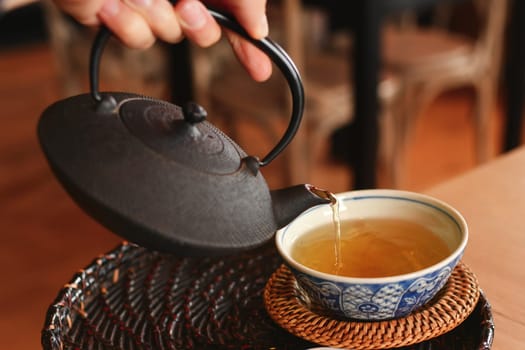 Hand pours green tea from a cast iron teapot into a cap