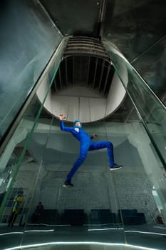 A man in overalls and a protective helmet enjoys flying in a wind tunnel. Free fall simulator.