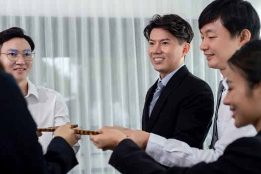 Closeup hand holding wooden gear by businesspeople wearing suit for harmony synergy in office workplace concept. Group of people hand making chain of gears into collective form for unity symbol.