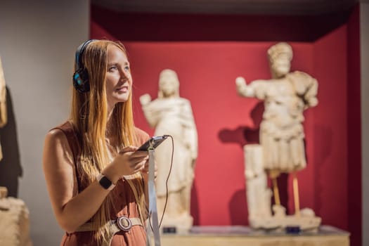Portrait of contemporary young woman looking at sculptures and listening to audio guide at museum exhibition.