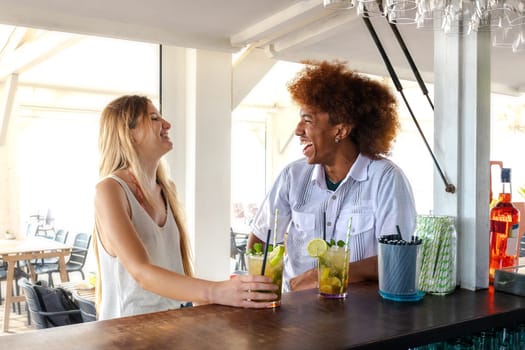 Young multiracial couple enjoying time together, laughing at a beach bar drinking mojito cocktails. Lifestyle and summertime concept.