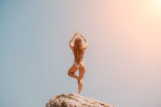 Woman meditating in yoga pose silhouette at the ocean, beach and rock mountains. Motivation and inspirational fit and exercising. Healthy lifestyle outdoors in nature, fitness concept.