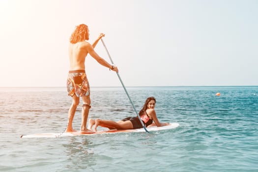 Sea woman and man on sup. Silhouette of happy young woman and man, surfing on SUP board, confident paddling through water surface. Idyllic sunset. Active lifestyle at sea or river
