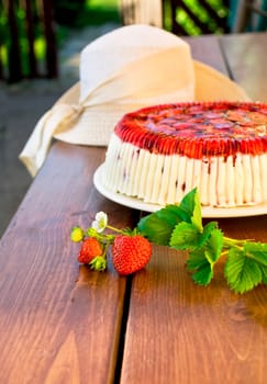 Cake with strawberries and whipped cream decorated with leaves on wooden background