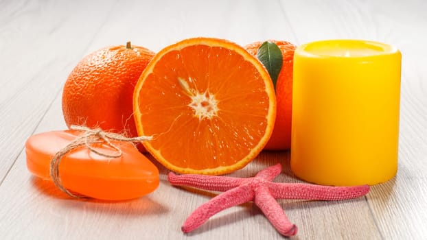 Cut orange with two whole oranges, soap, starfish and burning yellow candle on wooden desk. Spa products and accessories.