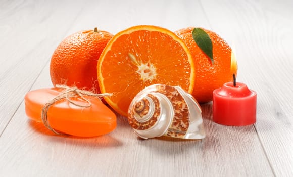 Cut orange with two whole oranges, soap, sea shell and burning red candle on wooden desk. Spa products and accessories.