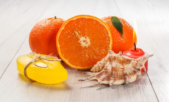 Cut orange with two whole oranges, soap, sea shell and burning red candle on wooden desk. Spa products and accessories.