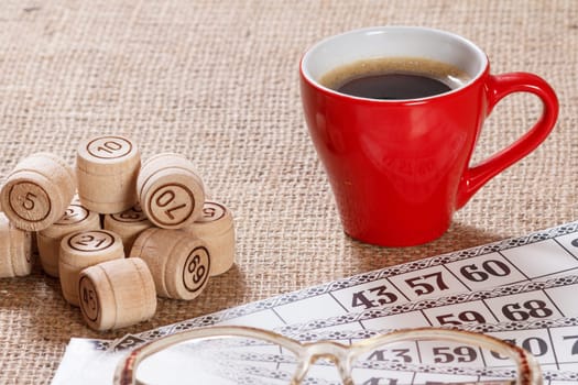 Board game lotto on sackcloth. Wooden lotto barrels and game cards for a game in lotto with red cup of coffee and glasses.