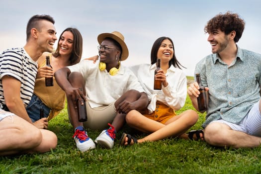 Diverse friends enjoying time outdoors. Multiracial young people having fun together drinking beer and laughing outdoors. Friendship concept.