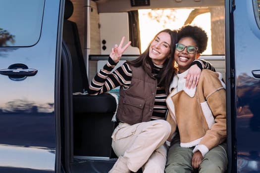 two young women in a camper van having fun and smiling looking at camera, concept of weekend getaway and female friendship, copy space for text