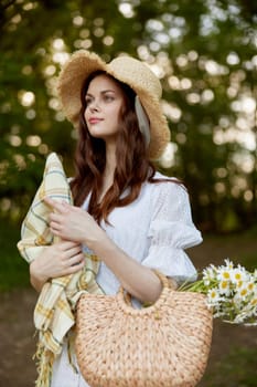 a happy, romantic woman stands in a light dress with a hat on her head and a plaid in her hands in the park. High quality photo