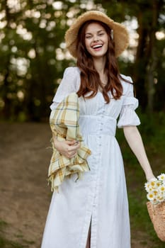 a happy, romantic woman stands in a light dress with a hat on her head and a plaid in her hands in the park. High quality photo