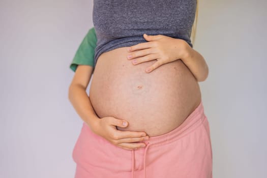 Young beautiful pregnant woman and elder son. The cute boy put his hands on his mother's belly. Expecting a baby in the family concept. Preparing an older child for a younger one.