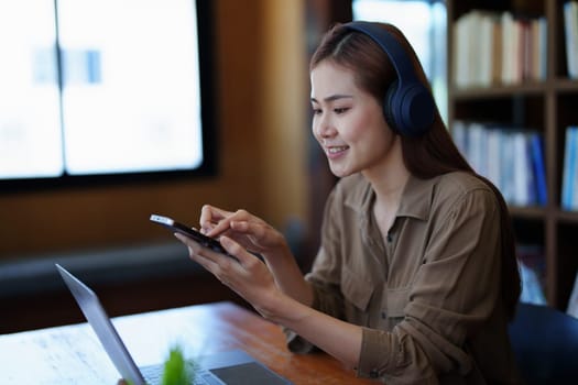 Portrait of a smiling Asian teenage girl wearing headphones and using a computer for online video conferencing in a library.