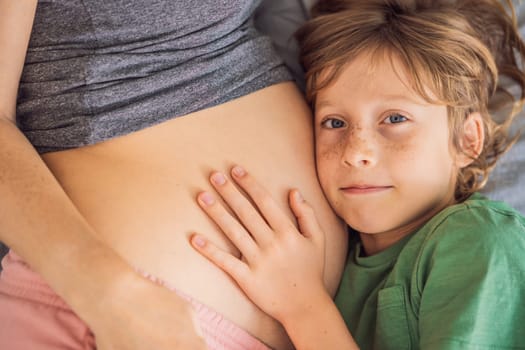 Young beautiful pregnant woman and eldest son. The cute boy leaned his ear against his mother's belly. Expecting a baby in the family concept. Preparing an older child for a younger one.
