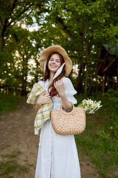 a happy woman in a light summer dress stands in nature with a wicker hat, a plaid and a basket with daisies. High quality photo