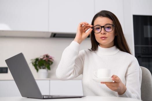 Young businesswoman adjusting her glasses and holding a cup of coffee, working at the home office.