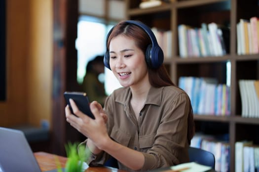 Portrait of a smiling Asian teenage girl wearing headphones and using a computer for online video conferencing in a library.