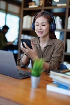 Portrait of a smiling Asian teenage girl wearing headphones and using a computer for online video conferencing in a library.
