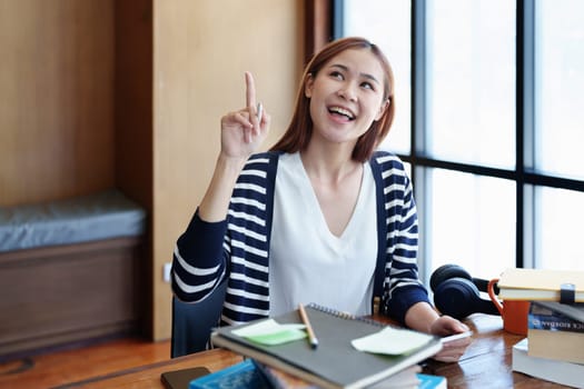 A portrait of a young Asian woman showing a smiling face and gesturing out ideas while using a tablet computer studying online at a library.