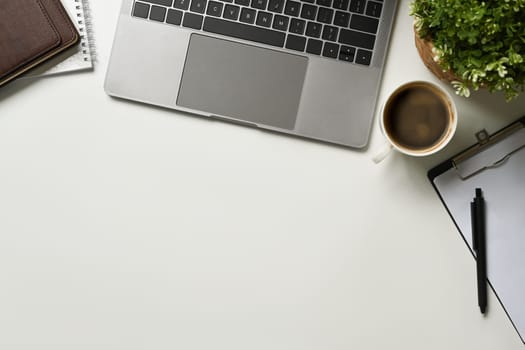 Modern white office desk table with laptop computer, cup of coffee and notebook. Top view with copy space, flat lay