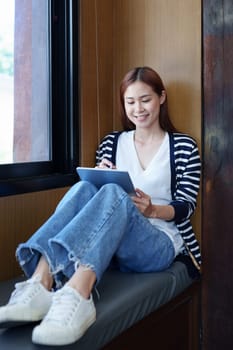 Portrait of a smiling Asian teenage girl using a tablet computer to study online via video conferencing.