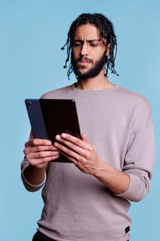 Confused arab man scrolling software app on digital tablet and surfing internet. Concentrated person navigating through application and browsing news online on portable gadget