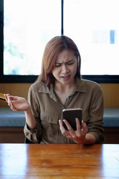 Portrait of a teenage Asian woman expressing dissatisfaction with her credit card being banned while using her phone for online shopping.