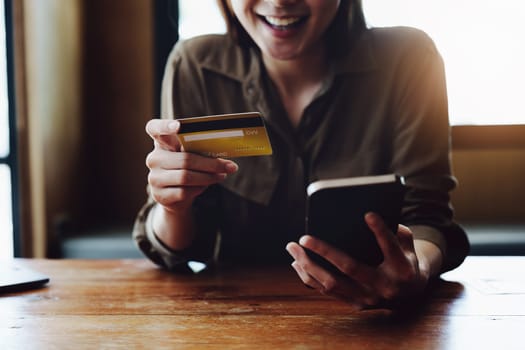 Portrait of young Asian woman using credit card and phone for online shopping.