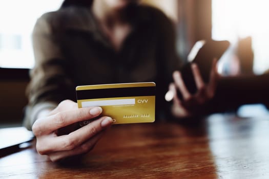 Portrait of young Asian woman using credit card and phone for online shopping.