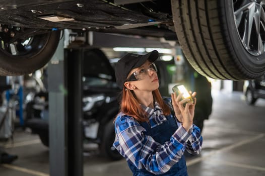 A female mechanic inspects a lifted car. A girl at a man's work