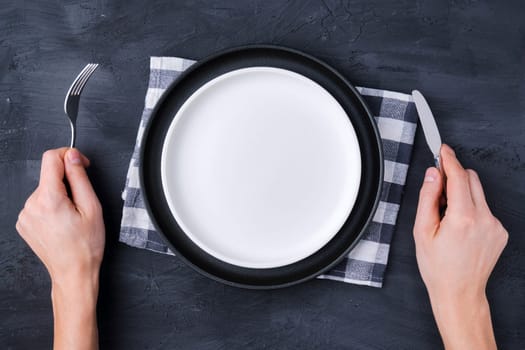 Man with a fork, a knife and an empty plate on a black background, top view